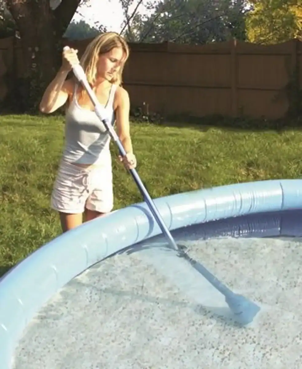 Un enfant utilise un aspirateur de piscine pour nettoyer la piscine.