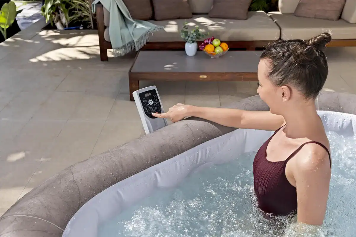 Une femme commande un spa gonflable avec une télécommande, se détendant dans l'eau.
