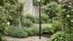 Douche extérieure W'eau Aurora dans un jardin avec des plantes vertes et des fleurs.