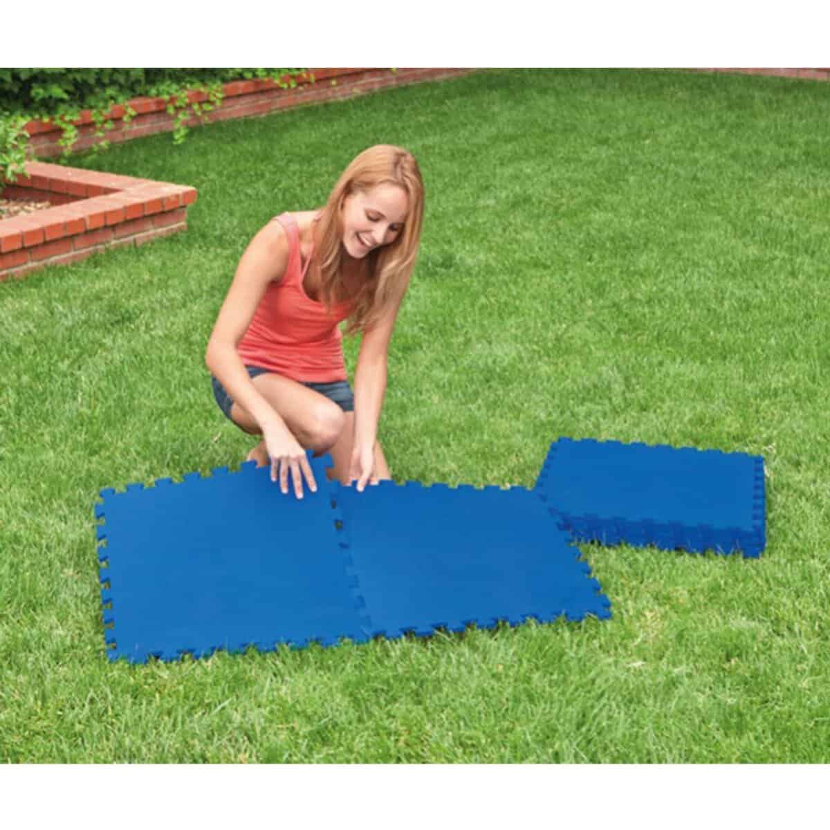 Un enfant qui gonfle et déplie un tapis de piscine gonflable dans le jardin.